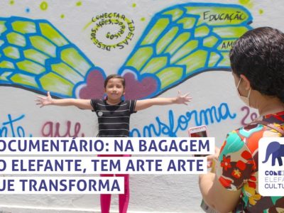 Criança de braços abertos em frente a mural com asas pintadas